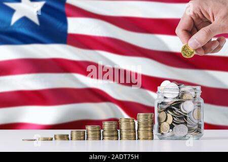 Business Mann mit Münzen, Glas, Liberia Flagge schwenkten im Hintergrund. Finanzen und Business Konzept. Spart Geld. Stockfoto