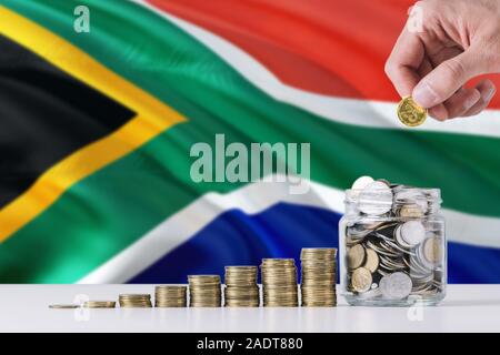 Business Mann mit Münzen, Glas, Südafrika Flagge schwenkten im Hintergrund. Finanzen und Business Konzept. Spart Geld. Stockfoto