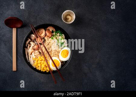 Ramen. Soba Nudeln mit Ei, Shiitake und enoki Pilze, Mais und Frühlingszwiebeln, geschossen von oben auf einen dunklen Hintergrund mit Stäbchen, Sake Stockfoto