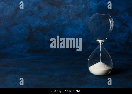 Die Zeit läuft. Eine Sanduhr mit nässen Sand, auf dunkelblauem Hintergrund mit Kopie Raum Stockfoto