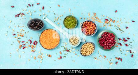 Hülsenfrüchte, Overhead Panorama-aufnahme auf blauem Hintergrund. Lebendige Impulse einschließlich bunte Bohnen, Linsen, Sojabohnen, Kichererbsen, flach Stockfoto