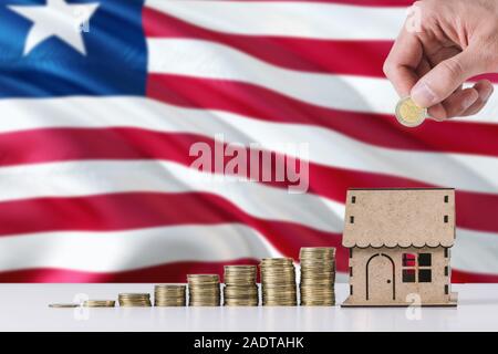 Mann mit Münzen in Holzhaus kässeli, Liberia Flagge schwenkten im Hintergrund. Geld sparen für die Hypothek. Stockfoto