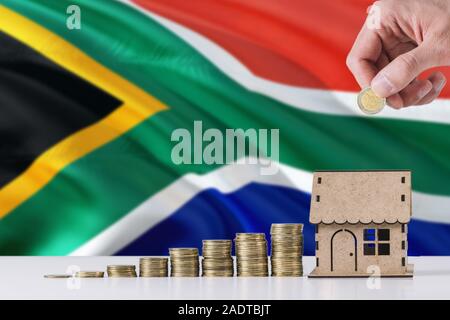 Mann mit Münzen in Holzhaus kässeli, Südafrika Flagge schwenkten im Hintergrund. Geld sparen für die Hypothek. Stockfoto