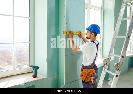 Ein Bauherr auf einer Leiter stehend installiert Trockenbau auf einer Baustelle Stockfoto