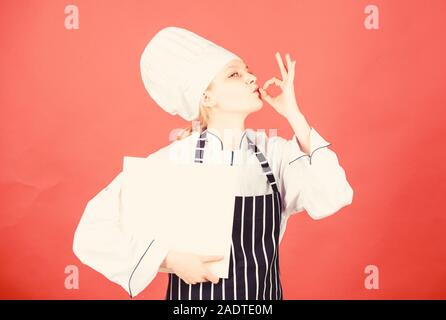 Glückliche Frau Kochen gesund essen von Rezept. Menü im Restaurant. Kulinarische nähren. Frau in Cook hat und Schürze. professioneller Koch in der Küche. Küche. Hausfrau mit Kochbuch. Die Auswahl von Lebensmitteln. Stockfoto