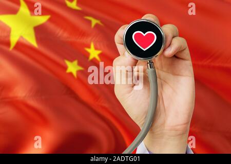 Arzt holding Stethoskop mit roten Liebe Herz. Nationale China Flagge Hintergrund. Healthcare System Konzept, medizinische Thema. Stockfoto