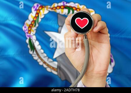Arzt holding Stethoskop mit roten Liebe Herz. Nationale Nördliche Marianen Flagge Hintergrund. Healthcare System Konzept, medizinische Thema. Stockfoto