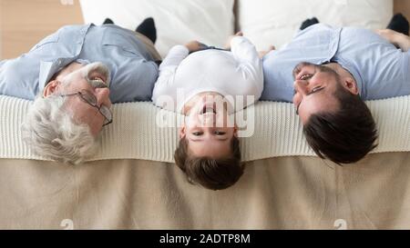 Großvater aufgewachsen, Sohn Enkel liegt auf dem Bett Köpfe unten Stockfoto