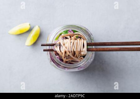 Soba Nudeln Salat, Suppe mit Gemüse, Tofu und Huhn in Gläsern. Grauer Hintergrund. Ansicht von oben Stockfoto