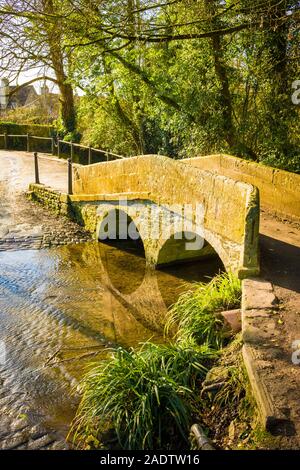 Die alte Stein Fuß-Brücke überspannt den langsam fließenden ByBrook stream, das Bestandteil eines Ford für vehicular Kreuzungen im ruhigen Dorf Lacock i Stockfoto