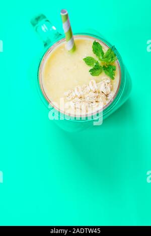 Mango, Banane, Ananas und Haferflocken Smoothie in das Glas mit Minze und Haferflocken. Leicht rosa unterlegt, Ansicht von oben Stockfoto