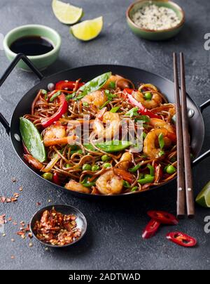 Stir Fry Nudeln mit Gemüse und Garnelen in Schwarz pan. Schiefer Hintergrund Stockfoto