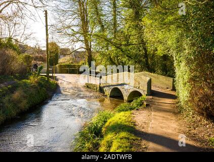 Die alte Stein Fuß-Brücke überspannt den langsam fließenden ByBrook stream, das Bestandteil eines Ford für vehicular Kreuzungen im ruhigen Dorf Lacock i Stockfoto