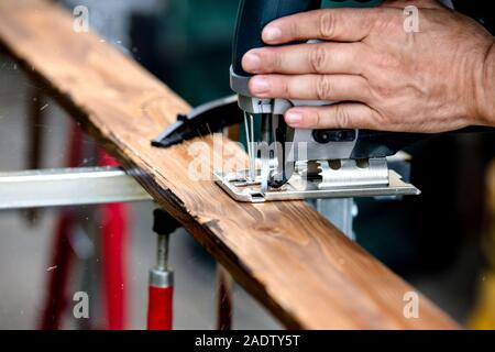 Nahaufnahme einer Hand mit Stichsäge, ein Brett mit einem elektrischen Hand gesägt ist sah Stockfoto