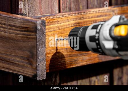 Glasierte board ist vorgebohrt. Akku Bohrer Bohrer ein Loch in einem braun glasiert Holzbrett Stockfoto