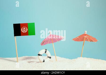 Miniatur Flagge Afghanistan am Strand mit bunten Sonnenschirmen und Schwimmweste. Travel Concept, Sommer Thema. Stockfoto