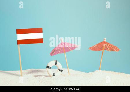 Miniatur Flagge Österreich am Strand mit bunten Sonnenschirmen und Schwimmweste. Travel Concept, Sommer Thema. Stockfoto