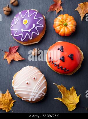 Donuts mit Halloween Dekoration, Sahnehäubchen auf schwarzem Schiefer Hintergrund. Ansicht von oben Stockfoto