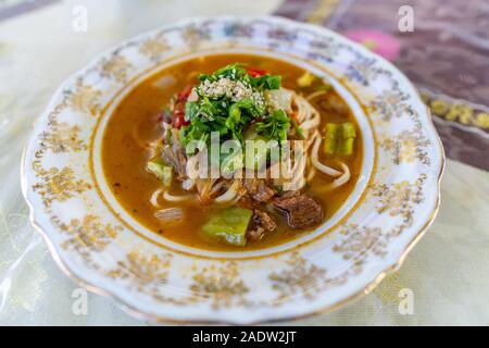 Traditionelle Mouthwatering Zentralasiatischen uigurischen Lagman Suppe, Hauptgericht mit Gemüse auf einem bunten Teller Stockfoto