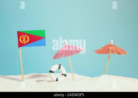 Miniatur Flagge Eritrea am Strand mit bunten Sonnenschirmen und Schwimmweste. Travel Concept, Sommer Thema. Stockfoto