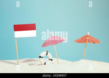 Miniatur Flagge Indonesien am Strand mit bunten Sonnenschirmen und Schwimmweste. Travel Concept, Sommer Thema. Stockfoto