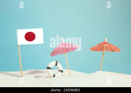 Miniatur Flagge von Japan am Strand mit bunten Sonnenschirmen und Schwimmweste. Travel Concept, Sommer Thema. Stockfoto