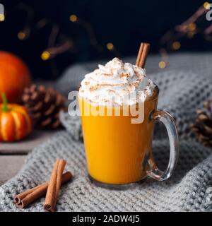 Kürbis Latte mit Gewürzen. Versoffenes Cocktail mit Schlagsahne. Strickschal Hintergrund Stockfoto