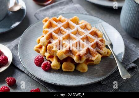 Belgische Waffeln mit Ahornsirup und frischen Himbeeren. Grauer Hintergrund. Close Up. Stockfoto