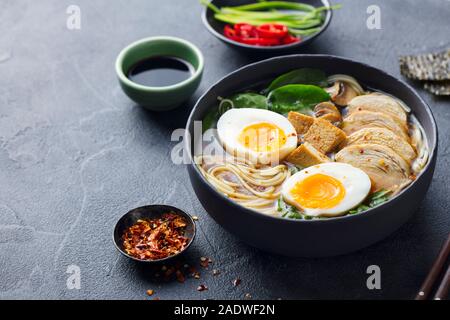 Asiatische Nudelsuppe, Ramen mit Huhn, Tofu, Gemüse und Ei in schwarz Schüssel. Schiefer Hintergrund. Kopieren Sie Platz. Stockfoto