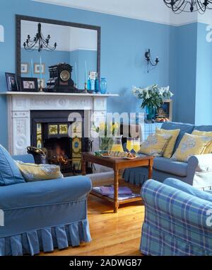 Rechteckiger Spiegel über dem Kamin in einem blauen Stadthaus Wohnzimmer mit blauen Sofas um einen hölzernen Couchtisch angeordnet Stockfoto