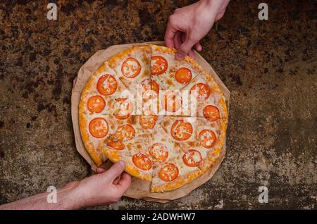 Pizza mit Käse und Tomaten mit Kopie auf eine ungewöhnliche brutale Metall Hintergrund mit Rost. Zwei Leute nehmen Scheiben pizza von zwei Seiten. Für mich Stockfoto