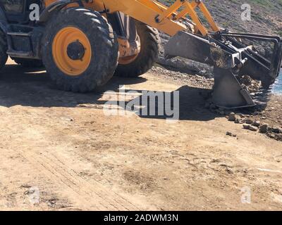 Gelbe Heckbagger plant eine Fahrbahn während der Straße Bauarbeiten. Erdbewegung, Ausgrabungen, Graben auf der felsigen Böden. Stockfoto