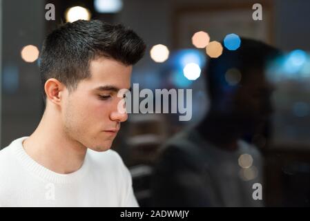 Junger Mann mit ernsten Ausdruck warten im Coffee Shop in der Nacht enttäuscht. Stockfoto