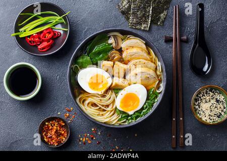 Asiatische Nudelsuppe, Ramen mit Huhn, Tofu, Gemüse und Ei in schwarz Schüssel. Schiefer Hintergrund. Ansicht von oben Stockfoto