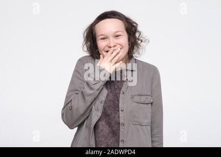 Ziemlich kaukasischen junge Frau schüchtern lachend über den Mund mit der Hand. Studio gedreht. Posititve Gesichts menschliche Emotion Stockfoto