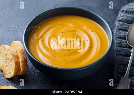 Kürbis, Karotten creme Suppe in eine Schüssel geben. Grauer Hintergrund. Nahaufnahme Stockfoto