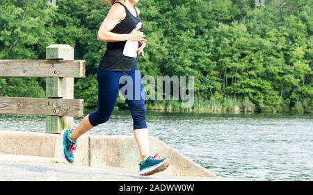 Eine Frau läuft ein 10-K-Rennen durch einen Park, über eine Brücke neben southards Teich mit Bäumen im Hintergrund. Stockfoto