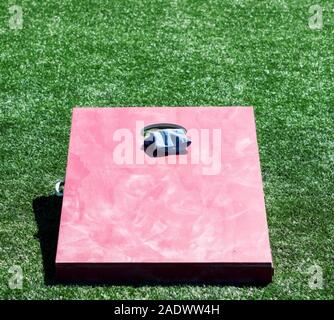 Eine handbemalte hausgemachte Rote cornhole Spiel wird auf einem grünen Rasenfeld mit einem blauen Bohnen schlecht in der Bohrung. Stockfoto