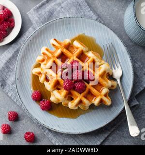 Belgische Waffeln mit Ahornsirup und frischen Himbeeren. Grauer Hintergrund. Ansicht von oben Stockfoto