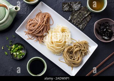 Sortiment japanischer Soba Nudeln mit Sauce und Beilagen. Schwarzer Schiefer Hintergrund. Ansicht von oben Stockfoto