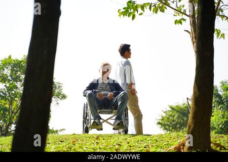 Jungen asiatischen erwachsener Sohn verbringt Zeit mit Rollstuhl Vater outdoor Stockfoto