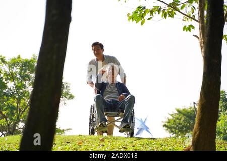 Jungen asiatischen erwachsener Sohn und Rollstuhl Vater Genießen der Natur im Park Stockfoto