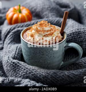 Kürbis Latte mit Gewürzen. Versoffenes Cocktail mit Schlagsahne. Grau gestrickt Hintergrund. Nahaufnahme Stockfoto