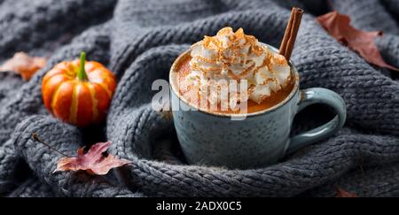 Kürbis Latte mit Gewürzen. Versoffenes Cocktail mit Schlagsahne. Grau gestrickt Hintergrund Stockfoto