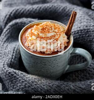 Kürbis Latte mit Gewürzen. Versoffenes Cocktail mit Schlagsahne. Grau gestrickt Hintergrund. Nahaufnahme Stockfoto