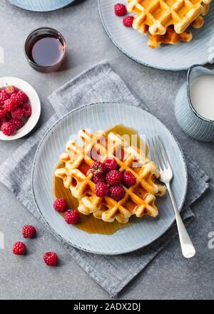 Belgische Waffeln mit Ahornsirup und frischen Himbeeren. Grauer Hintergrund. Ansicht von oben Stockfoto