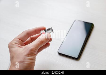 SIM-Fach Halter micro SD Card Slot Adapter in der Hand. Smart Phone im Hintergrund Stockfoto