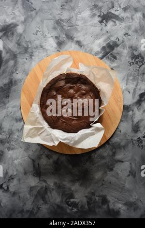 Frisch gebackene hausgemachte Schokolade Kuchen in Backpapier auf dunklen konkreten Hintergrund minimalistischen Stil Top View copyspace Stockfoto