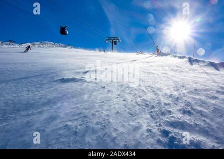 Sonniges Wetter im Skigebiet. Ein starker Wind treibt Schnee auf der Skipiste. Skilift im Hintergrund Stockfoto