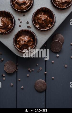 Hygge hausgemachte Desserts. Teig bereit für Schokolade Muffins backen mit Schokolade tropft in Backblech auf dunklem Hintergrund Draufsicht copyspace Stockfoto